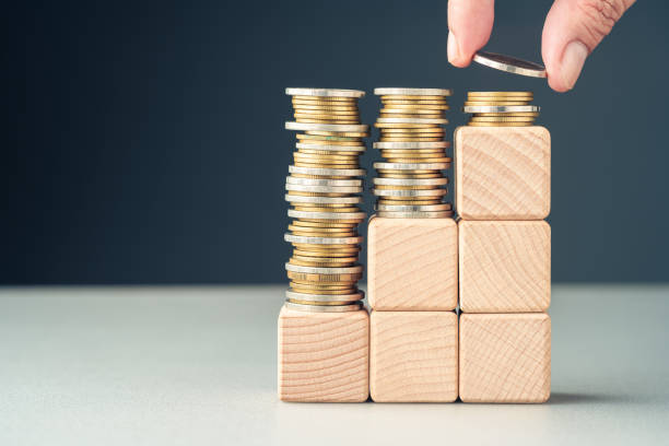 Hand add a few coins at the top of the final level built with wood cubes as step stairs, paying less in the long term, reducing cost, saving for the future, insurance, and investment, or subsidy money concept